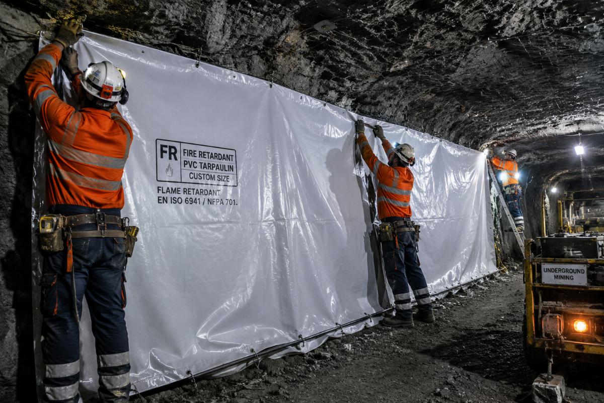 Workers installing custom sized FR fire-retardant PVC tarpaulin as underground mining site enclosure